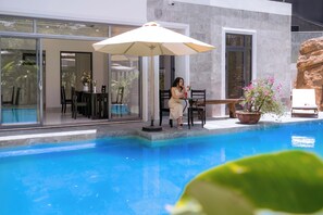 A poolside area with a table and chairs, a potted plant, and a large umbrella. - Vooc Signature Hotel Hoi An (Da Nang)