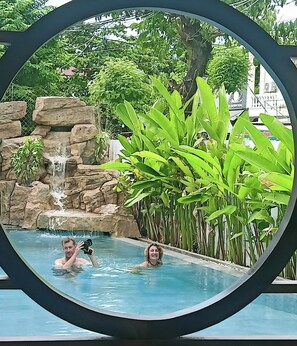 En swimmingpool med et vandfald og frodig beplantning.