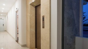 A modern hallway with a marble floor, an elevator, and a large arched window. - Vooc Signature Hotel Hoi An (Da Nang)