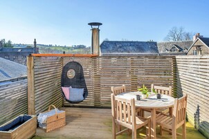 A wooden deck with a round table and chairs, a hanging chair, and a chimney.