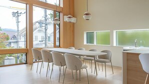 Un comedor moderno con una larga mesa y seis sillas, ventanas grandes con vidrio esmerilado y vistas al exterior.