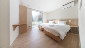 Una habitación de hotel moderna con una cama grande, un armario de madera y un ventanal corredero hacia el exterior.