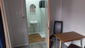 Une pièce avec une table en bois et deux chaises, un petit lavabo et une cabine de douche en verre.