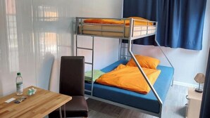 Un lit superposé avec une literie orange, une table en bois avec une chaise et une lampe sur une table de chevet.
