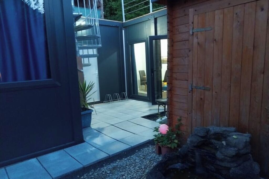 Una zona patio con pavimento piastrellato, recinzione in legno e un piccolo giardino con un fiore rosa.