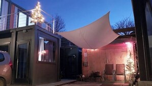 Un bâtiment moderne doté d’une grande marquise, avec une voiture garée devant, et une structure en bois avec une porte.