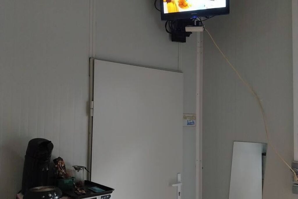 Une pièce avec un téléviseur fixé au mur, une porte et un tableau blanc.