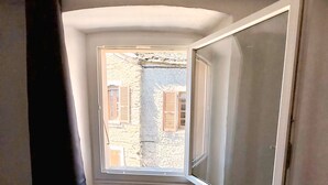 Quarto com teto inclinado, janela com persianas de madeira e piso de madeira.