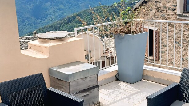 Terraço com mobiliário de vime, um vaso grande e vista para montanhas.