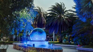 Una fuente con una esfera reflectante grande, rodeada de palmeras e iluminada con luces azules.