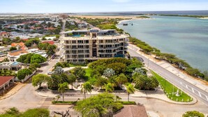 Un hotel de varios pisos con piscina en la azotea, rodeado de exuberante vegetación y vista a la playa.