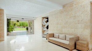 Un vestíbulo moderno con un sofá blanco, un diseño geométrico en la pared y una puerta de vidrio que da al exterior.