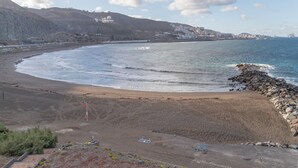 Eine Küstenlandschaft mit Strand, felsigem Ufer und Gebäuden in der Ferne.