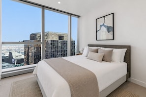Una habitación de hotel moderna con una cama grande, vistas a la ciudad y una obra de arte enmarcada en la pared.