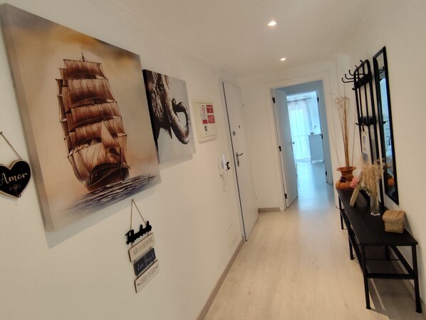 A hallway with a large ship painting, a heart-shaped sign, and a black bench with a vase.