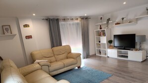 Ett modernt vardagsrum med en beige hörnsoffa, en platt-TV på ett vitt TV-bord och en blå matta.