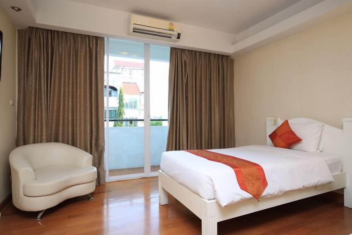 A hotel room with a bed, a chair, and a view through a glass door.