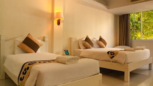 A hotel room with two beds, each with white bedding and brown pillows. There is a wall-mounted lamp on the left side and a window with curtains on the right. - Welnez World Residence Pattaya (Pattaya)