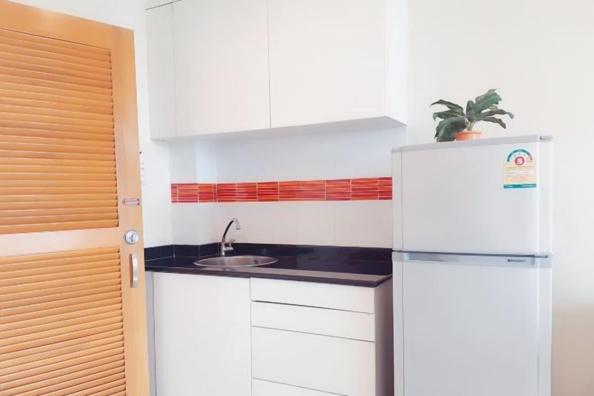 A kitchen with white cabinets, a black countertop, a sink, and a refrigerator with a plant on top.