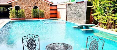 A pool area with two metal chairs and a table, surrounded by stone walls and greenery.