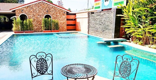 A pool area with two metal chairs and a table, surrounded by stone walls and greenery.