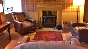 A cozy living room with a fireplace, leather armchairs, a patterned rug, and a plaid wallpaper.