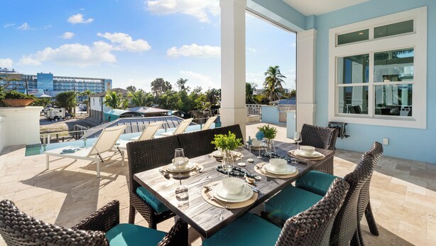 A sunlit patio with a dining table set for four, overlooking a swimming pool and a cityscape. - Seaside Villa Aqua luxury 4-bedroom villa in Fort Myers Beach incredible view (Fort Myers Beach)