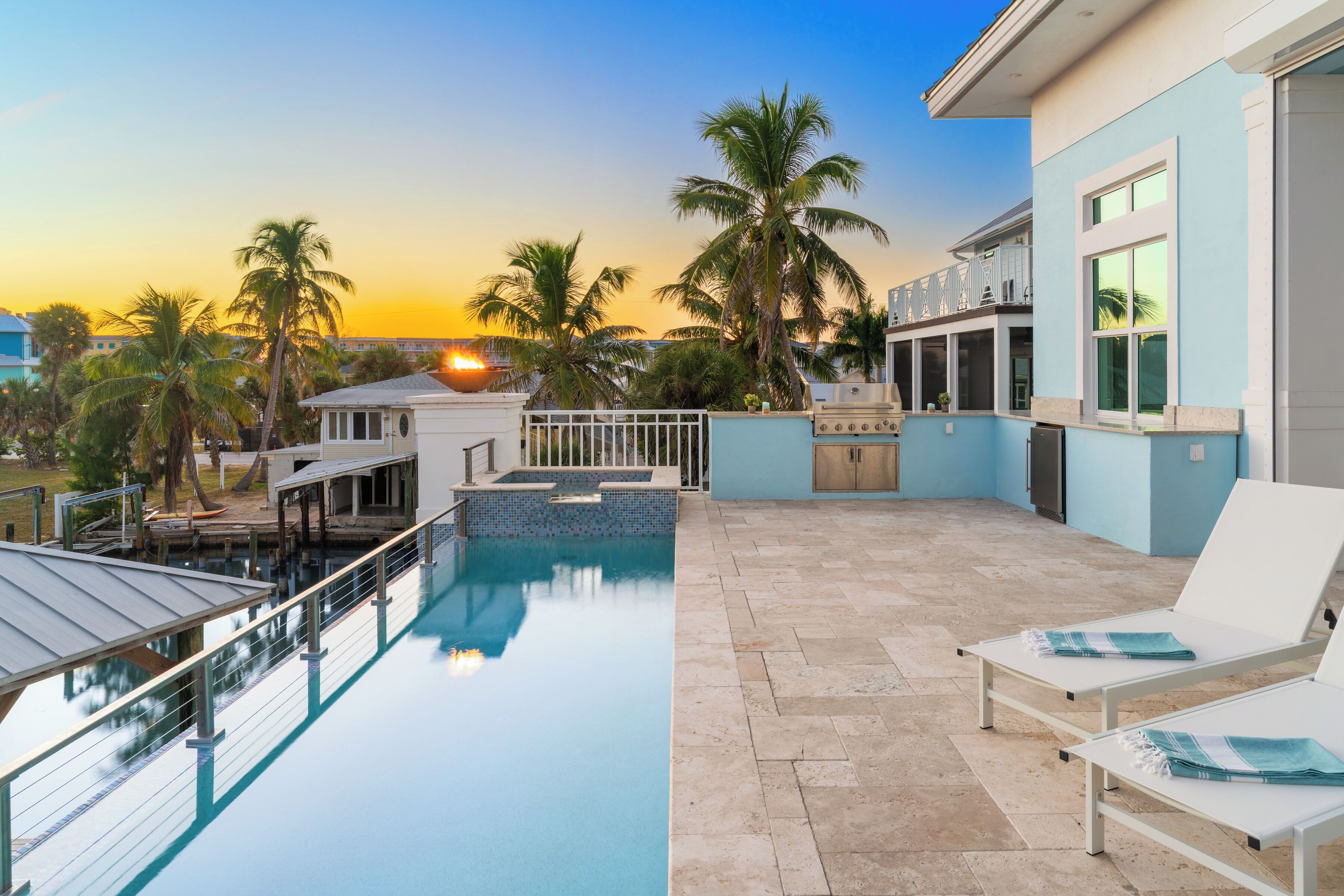 Una piscina en la azotea con vistas a la puesta de sol, palmeras y un área de barbacoa.