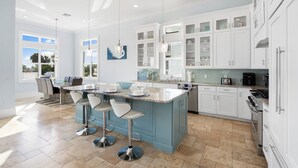 A modern kitchen with white cabinets, a blue island, and a dining area with bar stools. - Seaside Villa Aqua luxury 4-bedroom villa in Fort Myers Beach incredible view (Fort Myers Beach)