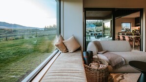 Una sala de estar moderna con un amplio ventanal que ofrece una vista panorámica de un paisaje con césped y montañas.