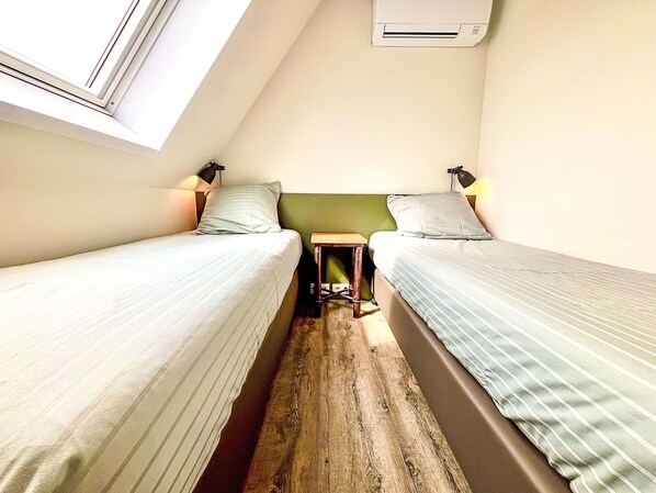 Una habitación pequeña y triangular con dos camas individuales, suelo de madera y techo inclinado.