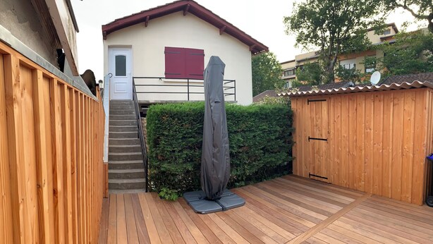 A wooden deck with a covered seating area, a staircase leading to a building with a red shutter, and a hedge in the background. - In the heart of Andernos-les-Bains, 200 m from the beach (Andernos-les-Bains)
