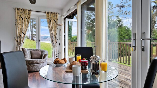 Een moderne kamer met een glazen tafel, een bank en een zithoek met ontbijtartikelen.