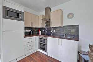 A kitchen with white cabinets, a microwave, a stove, and a sink. - Cottage on Kintyre Peninsula by Ellary Burn (Lochgilphead)