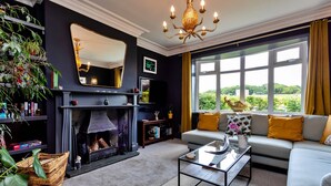 A living room with a fireplace, sofa, and large windows with a view. - Watchtower in Cornwall With Sea Views (Newbiggin-by-the-Sea)