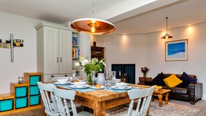 A dining area with a wooden table, white chairs, and a hanging light fixture. - Watchtower in Cornwall With Sea Views (Newbiggin-by-the-Sea)