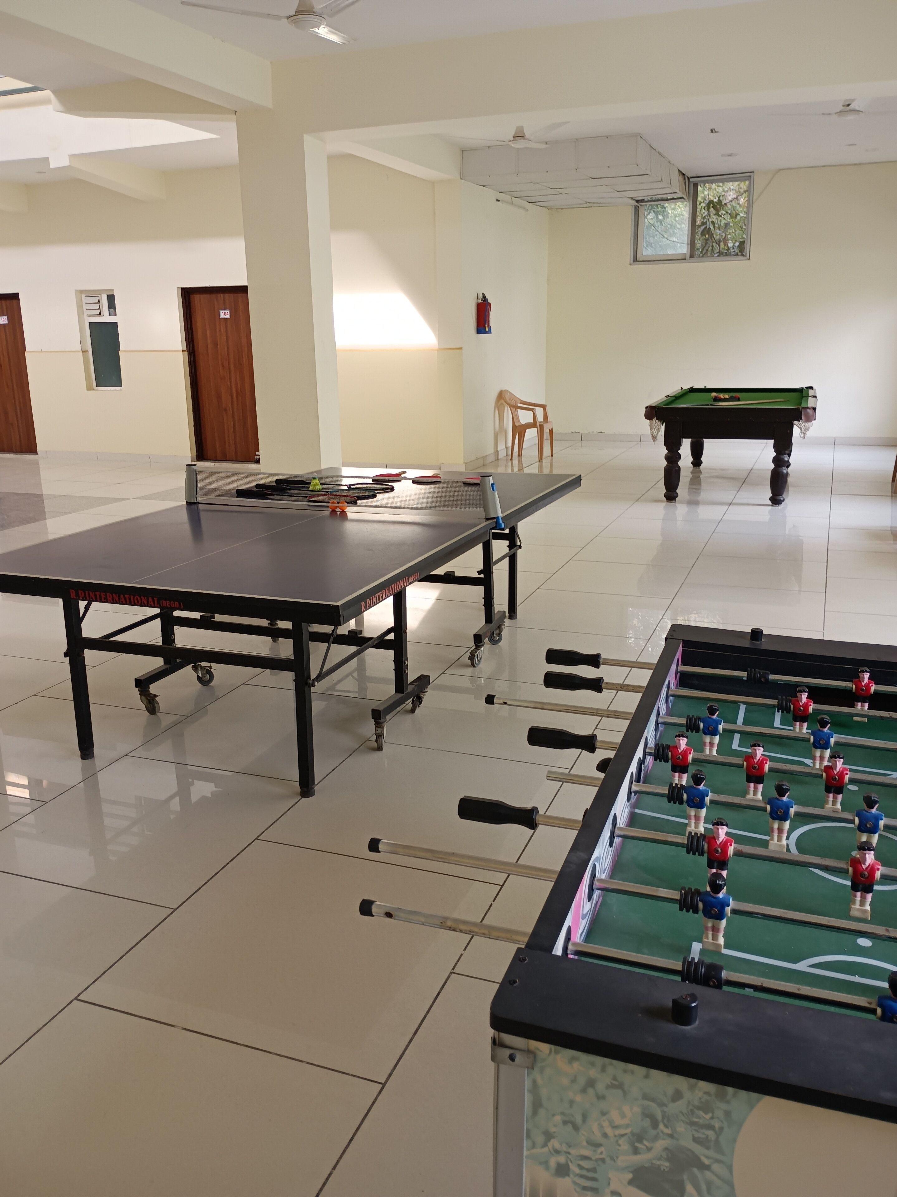 Un grand espace intérieur comprenant une table de baby-foot, une table de ping-pong et une table de billard.