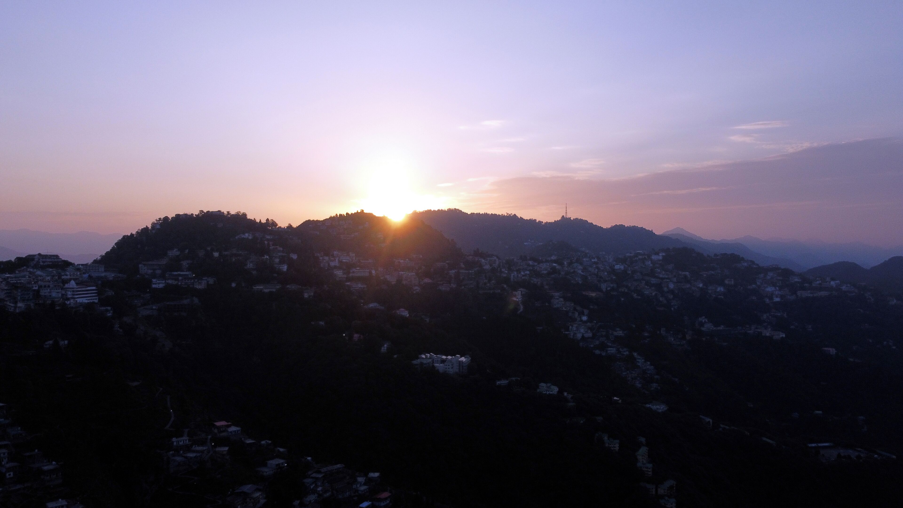 A mountainous landscape with a sunrise or sunset over a densely populated area.