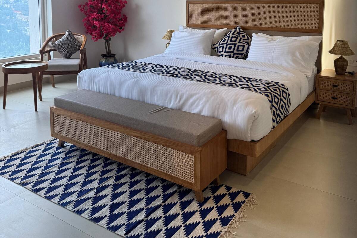 Une chambre à coucher moderne avec un grand lit, un banc, une chaise, une petite table et une table de chevet.