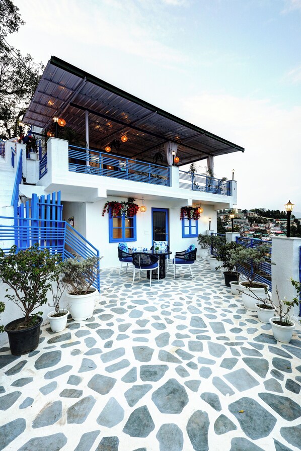 Un bâtiment à deux étages aux couleurs bleu et blanc, doté d’un revêtement de sol en pierre, d’un espace extérieur aménagé pour s’asseoir et de plantes en pot.