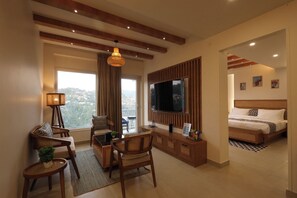 Una sala de estar moderna con un televisor grande, asientos cómodos, un balcón con vistas y un dormitorio independiente con cama y obras de arte.