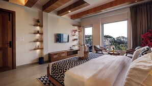 A modern hotel room with a large bed, a TV, a balcony with a city view, wooden beams on the ceiling, and built-in shelves.