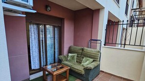 A small outdoor living area with a sofa, a glass coffee table, and a sliding glass door.