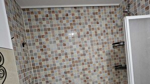 A bathroom with a tiled shower wall, a white bathtub, and a toilet.