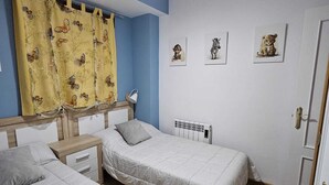 A room with two single beds, a ceiling fan, a radiator, and three wall-mounted animal pictures.