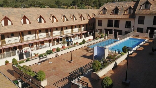 A hotel with a swimming pool, multiple balconies, and a courtyard with potted plants.