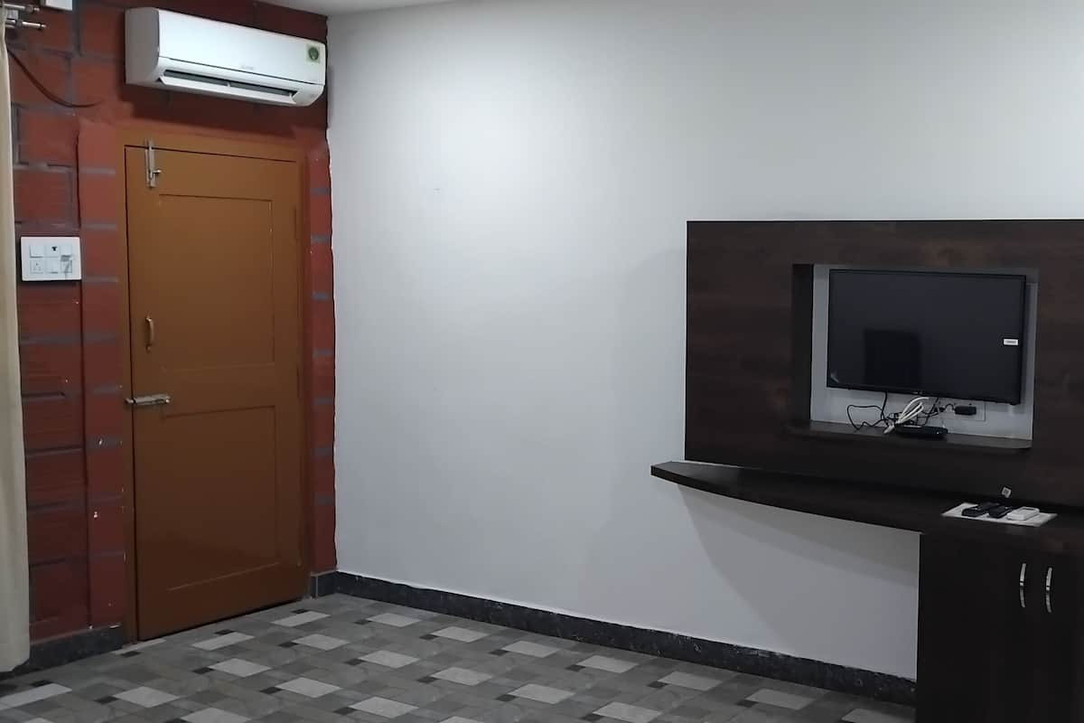 A room with a wooden door, an air conditioning unit, a flat-screen TV mounted on a dark wooden wall, and a small shelf below the TV.