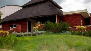 A building with a thatched roof and red brick walls, surrounded by well-maintained greenery.