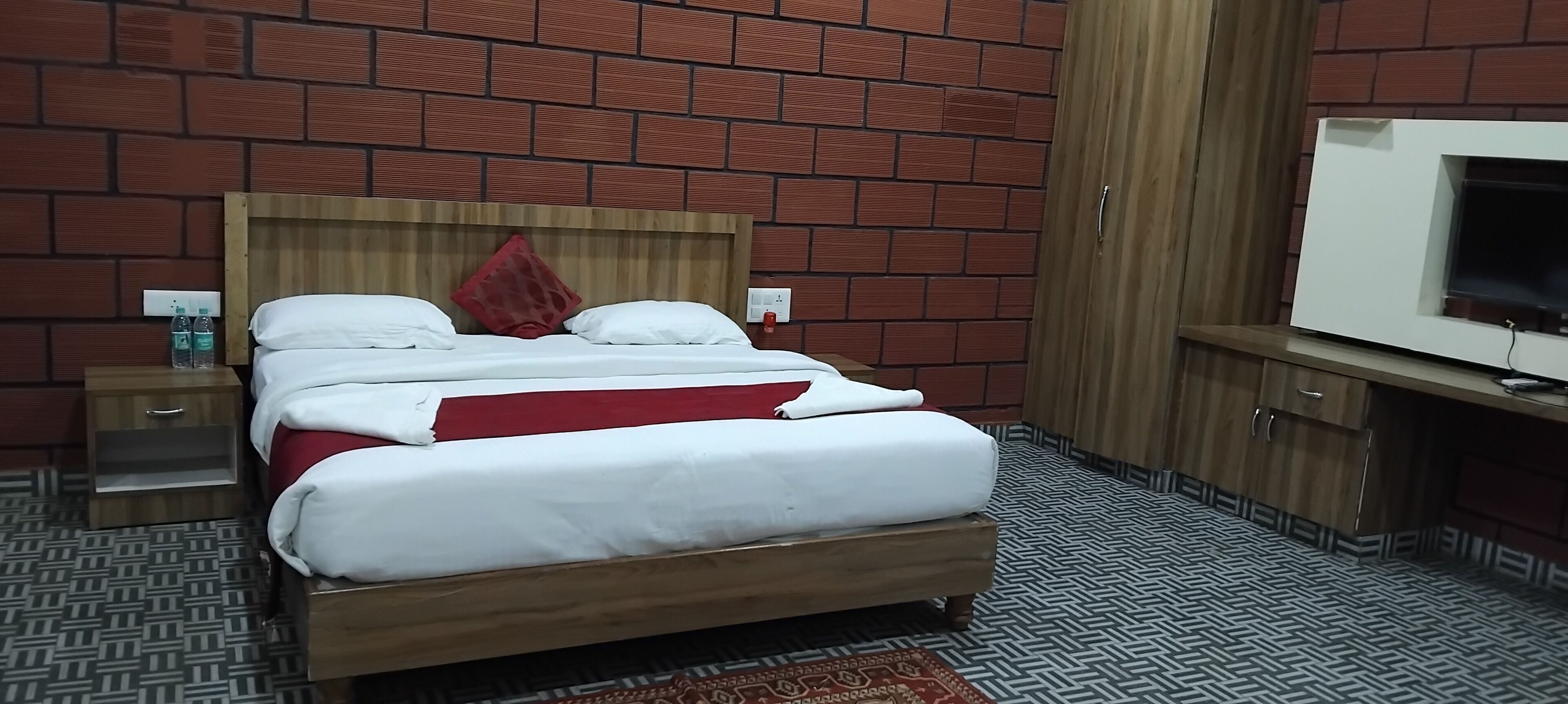 Une chambre d’hôtel avec un lit en bois, une télévision et un mur décoré d’un motif en briques.