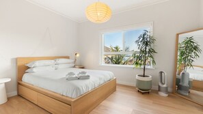 A modern bedroom with a wooden bed, a bedside lamp, a large window, and a potted plant.